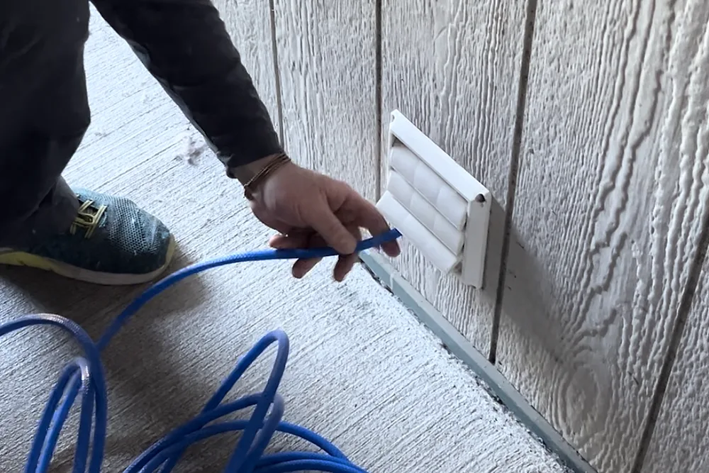 A Ventz technician feeding a compressed-air line into an exterior dryer vent hood