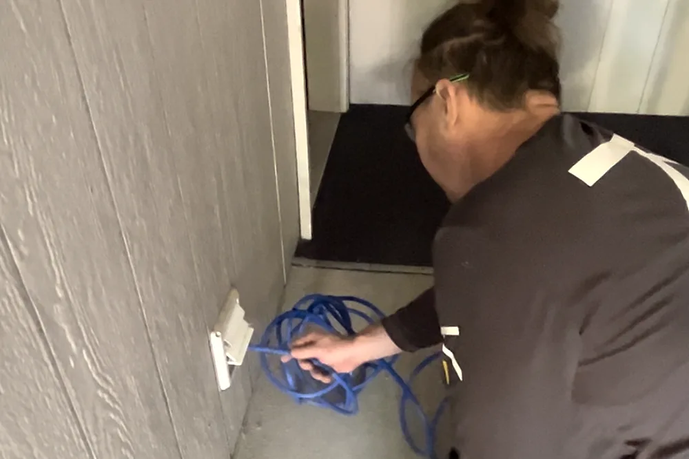A Ventz technician cleaning a ground-floor dryer vent in an apartment breezeway